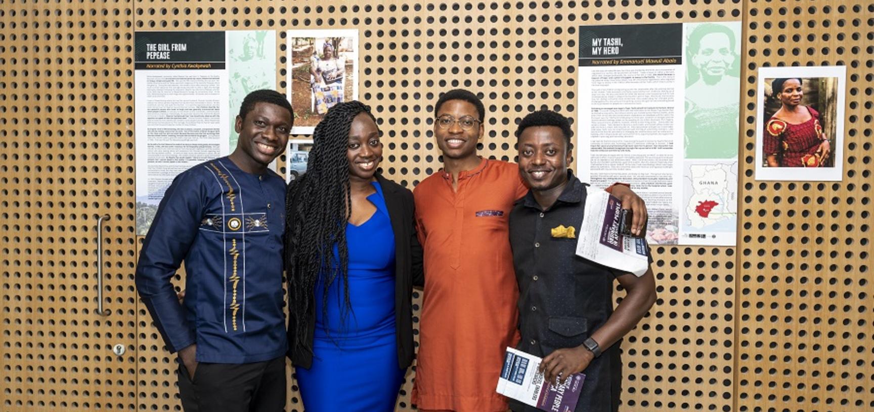 4 people smile at the camera in front of the poster exhibit