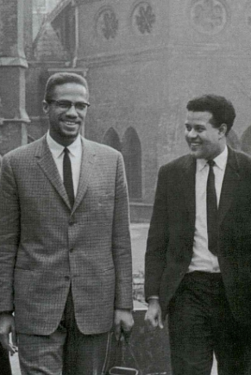 Black and white photograph of Malcom X and another man, smiling with Oxford buildings in background