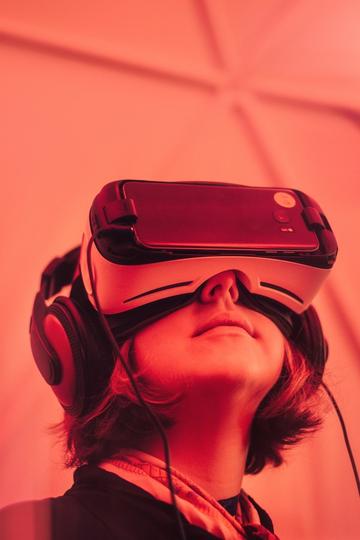 Pink tinted photo of a young girl wearing a VR headset and big headphones