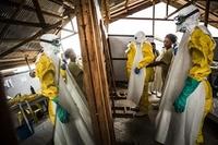 Several people getting dressed in hazmat suits and PPE in a barn-like building
