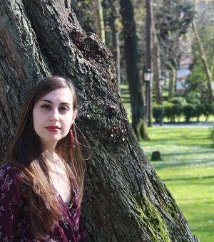 rocio riestra camacho, stood in front of a tree wearing a purple top. There are more trees and a lamppost in the background. 